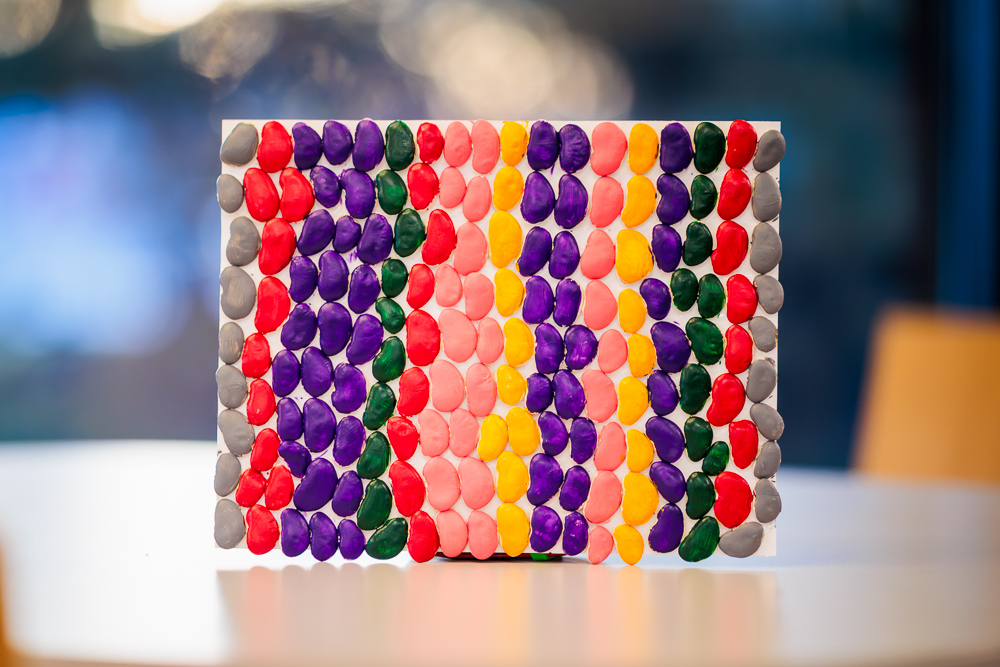 example of the craft being made, lime beans painted in different colors arranged by color in lines to create a piece of art inspired by Alma Thomas