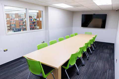 A small room that has a large conference table with 14 chairs and a television on the back wall.